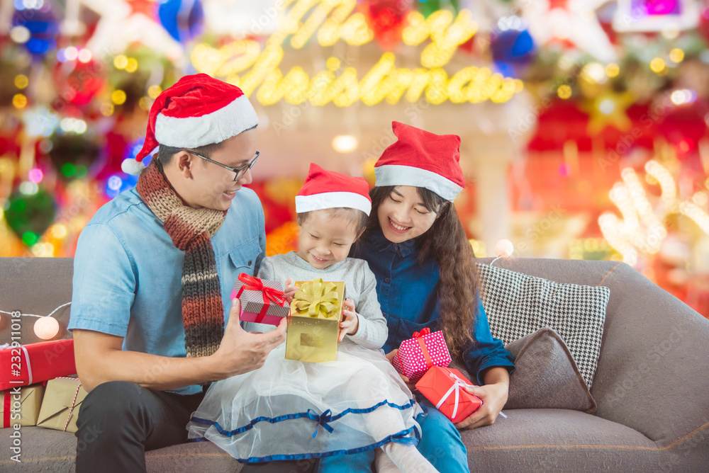 Little asian girl and her parents open christmas gifts box on sofa at home Little asian girl and her parents open christmas gifts box on sofa at home