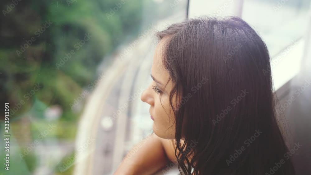 Young brunette pretty woman looking through the window. urban city view with buildings roads. slow motion. 3840x2160 Young brunette pretty woman looking through the window. urban city view with buildings roads. slow motion. 3840x2160
