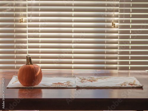 Pumpkin on a fall holidays themed placemat on top of a small brown wood table