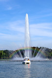 rainbow on fountain with people riding duck boat in lake of park with bluesky background