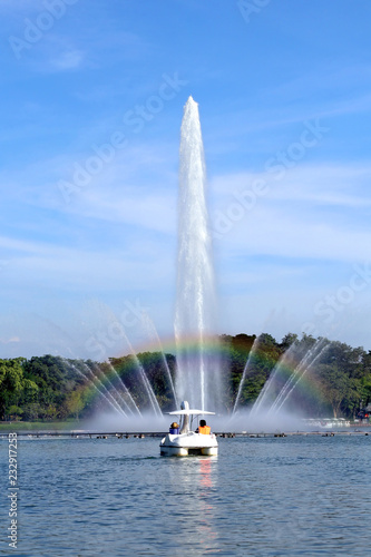 rainbow on fountain with people riding duck boat in lake of park with bluesky background