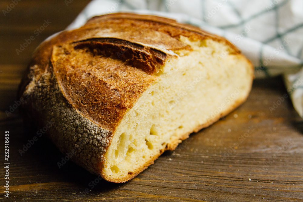 Fresh loaf of bread on the dark wooden table with a towel. Homemade bakery Fresh loaf of bread on the dark wooden table with a towel. Homemade bakery