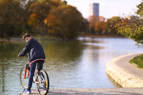 boy ride bicycle on city park lake background fall landscapce