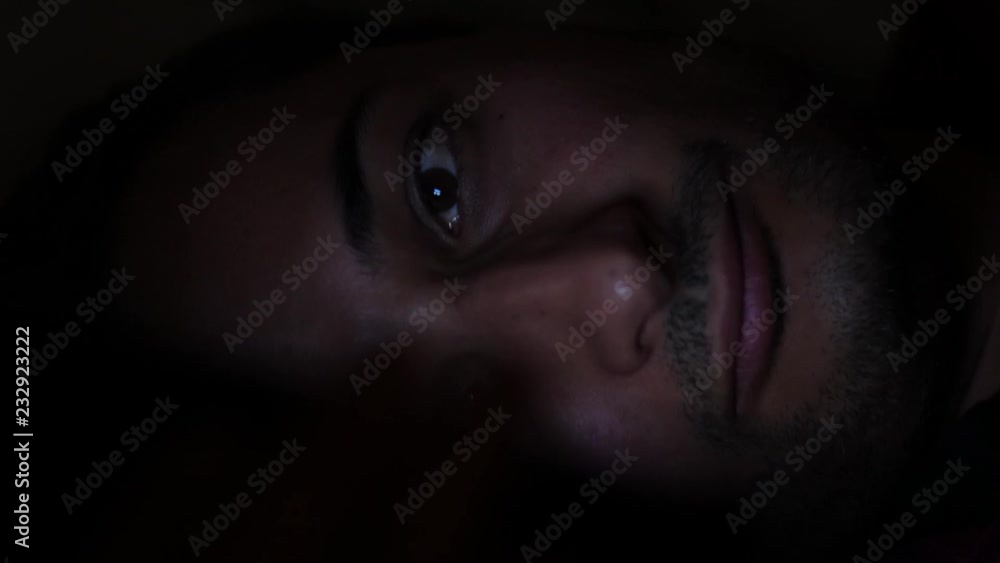 Man laying on the bed use smartphone in the dark Unshaven face and tired eyes Man laying on the bed use smartphone in the dark Unshaven face and tired eyes