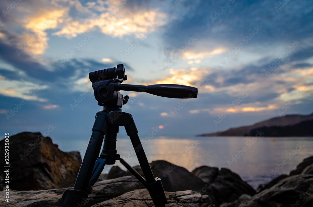 Low key shot of a tripod placed on rocks during sunrise. Low key shot of a tripod placed on rocks during sunrise.