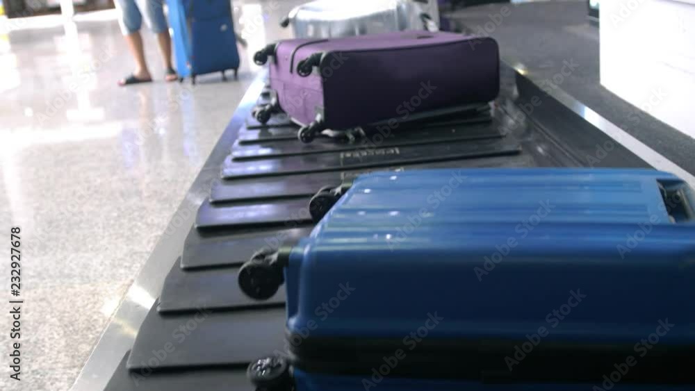 Airport baggage claim with luggage spinning around conveyor. Blurred man taveler takes her