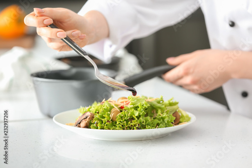 Young female chef dressing tasty salad in kitchen, closeup