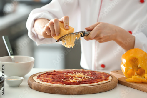 Young female chef cooking tasty pizza in kitchen, closeup
