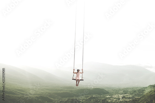 surreal moment of a woman having fun on a swing hanging from the sky photo