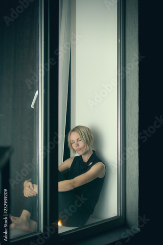 Sad woman on the windowsill looks out the window. © Konstiantyn Zapylaie