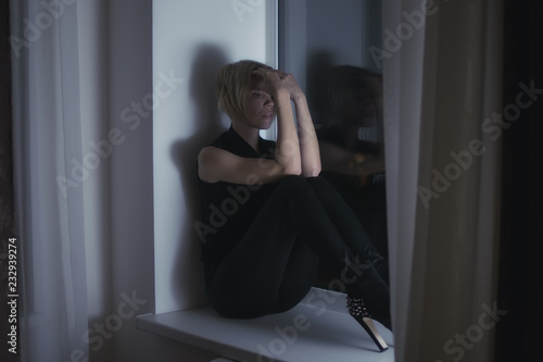 Sad woman on the windowsill looks out the window.