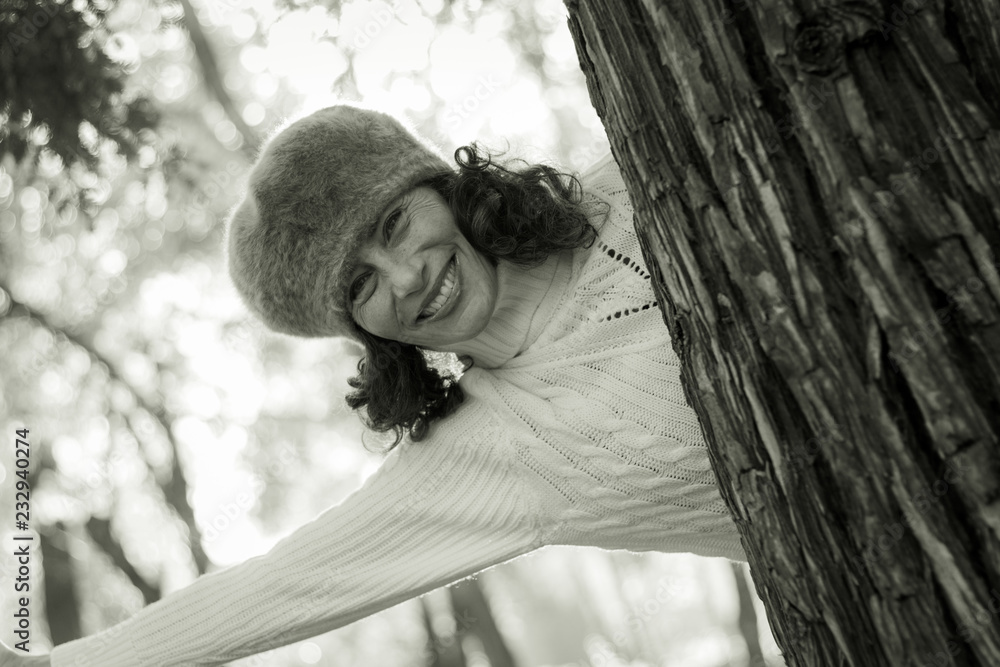 Graceful mature woman with hairy winter hat appears behind tree in the  park. Playful middle aged lady enjoying autumn season outdoors. Black and  white photography foto de Stock | Adobe Stock
