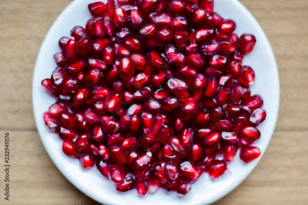 Pomegranate fruit (Latin: Punica granatum) is an exotic fruit with many vitamins and antioxidants. It is used within fruit juices and medicine. Top view of the fruit seeds on a white dish on the table Pomegranate fruit (Latin: Punica granatum) is an exotic fruit with many vitamins and antioxidants. It is used within fruit juices and medicine. Top view of the fruit seeds on a white dish on the table