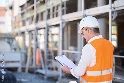 Architekt, Mann, Bauleiter auf der Baustelle mit klemmbrett und Plan von hinten