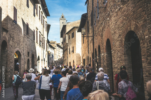 Crowd of tourists people walk together stretched and with the street full in San Gimignano near Siena in Tuscany, Italy. Vacation and culutre in a medieval city full of history photo