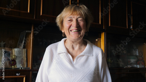 Russian senior smiling to camera in her home, old furniture in background, close up	