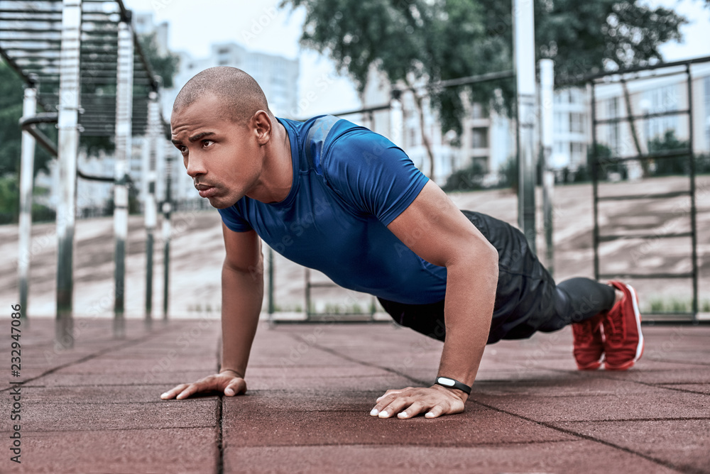 Fototapeta premium African man is doing plank at open air gym near the park