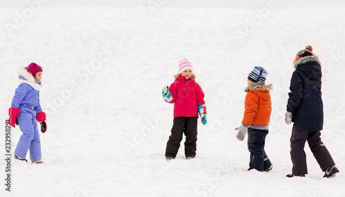 childhood, leisure and season concept - group of happy little kids in winter clothes playing outdoors