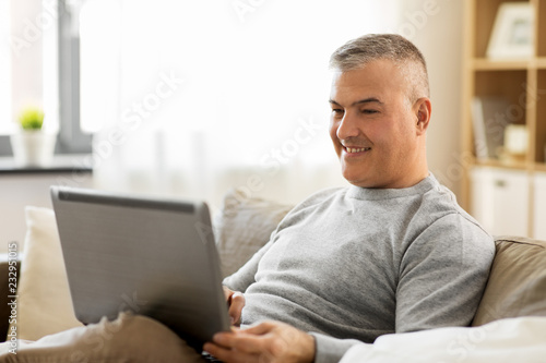 technology, people and lifestyle concept - man with laptop computer sitting on sofa at home
