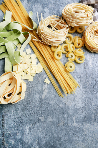 Mixed types and shapes of italian pasta on grey stone, background photo