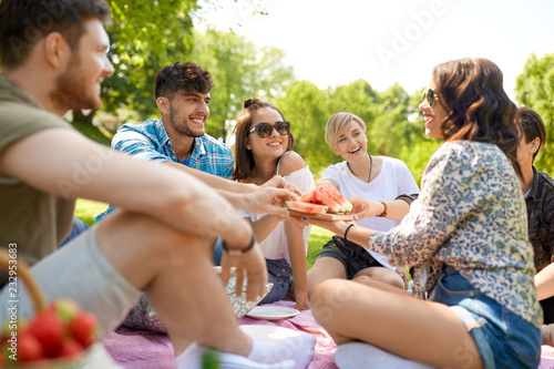 friendship, leisure and food concept - group of happy friends sharing watermelon at picnic in summer park