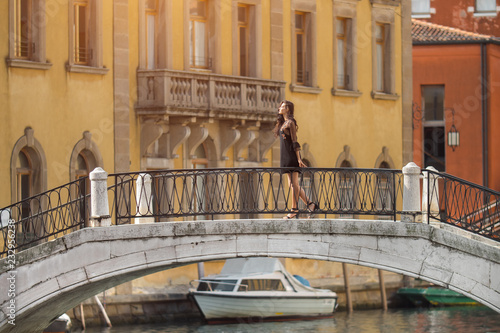 Travel to Italy. Girl standing on the bridge in Venice. Beautiful well-dressed woman posing on a bridge over the canal in Venice, Italy. Europe travel vacation. Woman traveling to Venice.