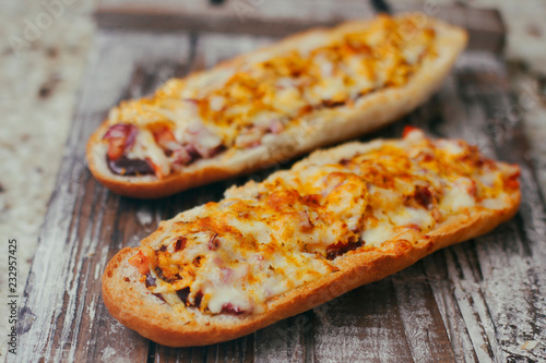 A couple of traditional french split baguettes with cheese and other complex filling. On wooden retro background stand tray.
