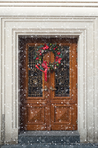 Vintage wooden door decorated with christmass wreath in snowy weather. Fragment of facade of the historical building at the centre of Lviv, Ukraine.