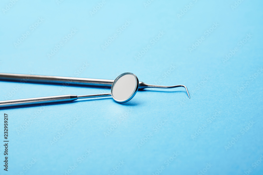 close up view of dental mouth mirror and probe on blue surface close up view of dental mouth mirror and probe on blue surface