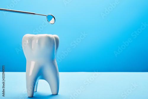 close up view of tooth model and dental mouth mirror on blue backdrop