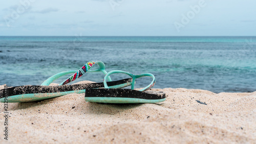 Colorful flip flops on a white sand beach with turquoise water. Summer vacation concept.