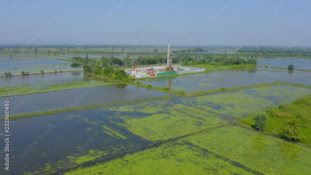 Oil and gas land drilling rig onshore in the middle of a rice field aerial view from a drone