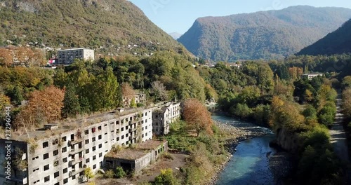 aerial motion along wonderful blue river with multi-storey houses on bank in ghost town among autumn trees