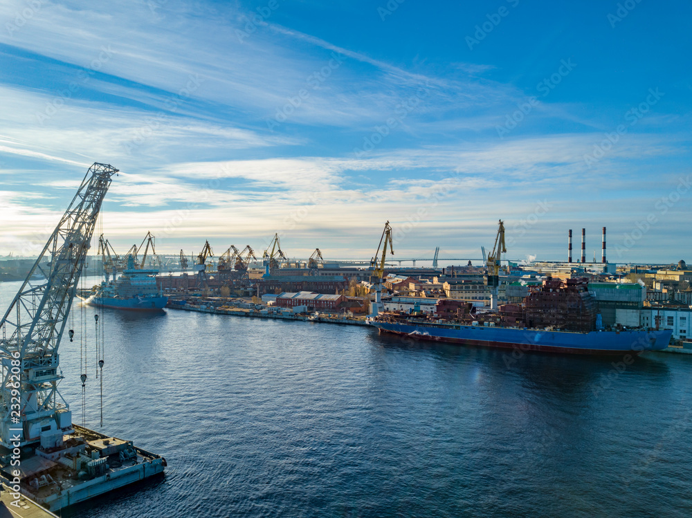 Aerial; drone view of port with shipyard silhouettes on the horizon; industrial cityscape in sunny weather with blue sky; process of ship repairing, logistic import export and transport background