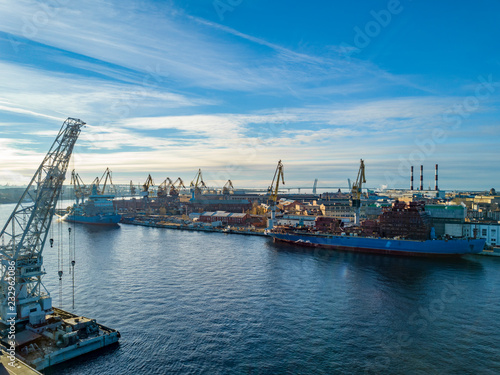 Aerial; drone view of port with shipyard silhouettes on the horizon; industrial cityscape in sunny weather with blue sky; process of ship repairing, logistic import export and transport background