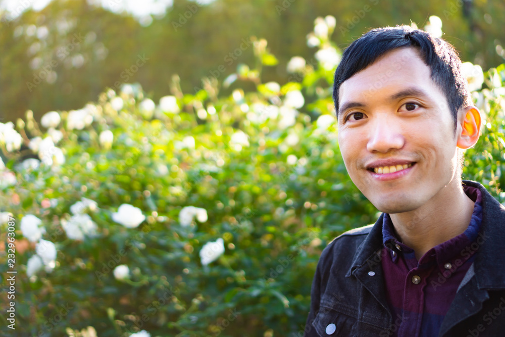 Portrait of young southeast asian man smiling and laughing happily on white roses background under the light of sunset in autumn Portrait of young southeast asian man smiling and laughing happily on white roses background under the light of sunset in autumn