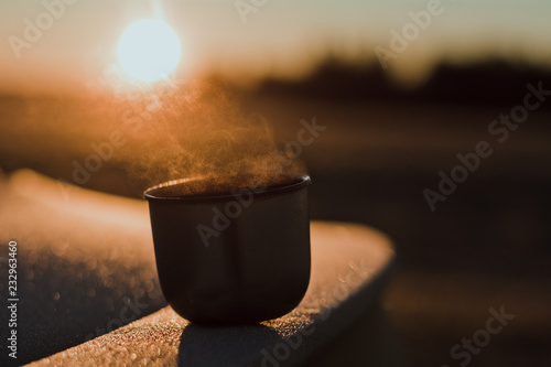 Steam from a hot tea mug from a thermos, which is illuminated by the winter morning sun in the light. Calm