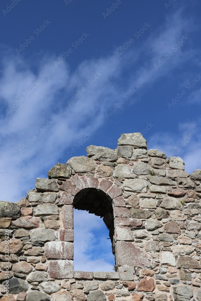 Window opening in olde stone wall against blue sky