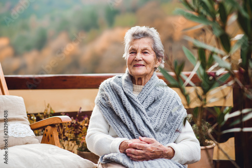 An elderly woman sitting outdoors on a terrace on a sunny day in autumn.