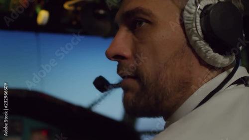 Close up shot of male pilot in headset sitting in cockpit of flying airplane and talking to aircraft captain off camera