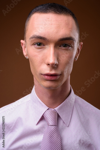 Young handsome androgynous businessman against brown background