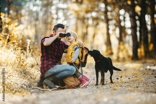 A mature father with a dog and a toddler son in an autumn forest, using binoculars. photo