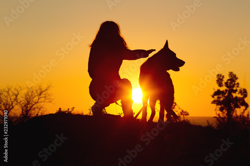 silhouette woman walking with a dog in the field at sunset, girl stroking pet sitting near on nature