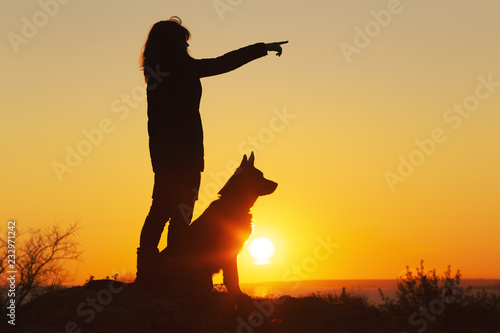 silhouette woman walking with a dog in the field at sunset  a girl showing her pet target ahead on the nature