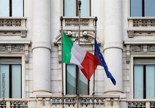 Italian flag hanging down next to deflated EU flag in the wind