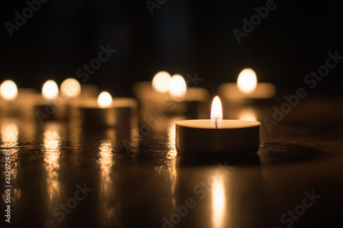 Small glowing candle on the floor on background of group of candles. Horizontal view