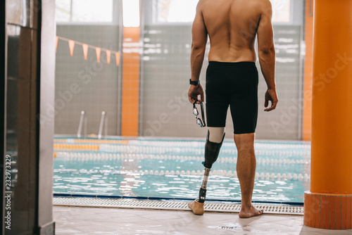 cropped shot of sportsman with artificial leg standing in front of indoor swimming pool