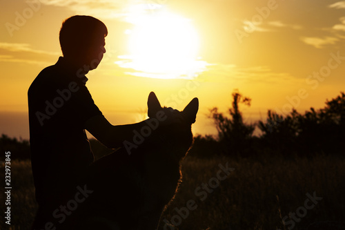 Fotografie silhouette of a man and a dog watching the sun set on the horizon in a field, bo