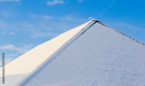 Snow on the roof of the house against the blue sky