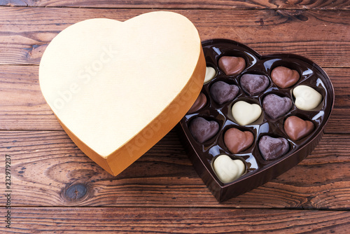 Heart shaped box with heart shaped dark and light chocolate truffles on wooden table